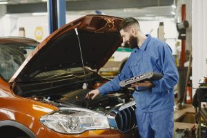 mechanic inspecting under hood of vehicle in auto shop