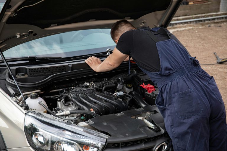 mechanic working under the hood of vehicle outside