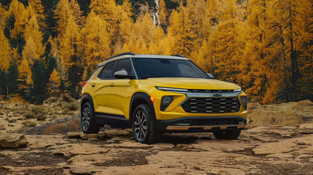 Yellow Chevy Trax, parked on a rugged ground in front of a scenic fall tree background.