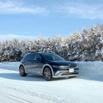 black electric hyundai Kona parked in snow with snow covered trees in the background