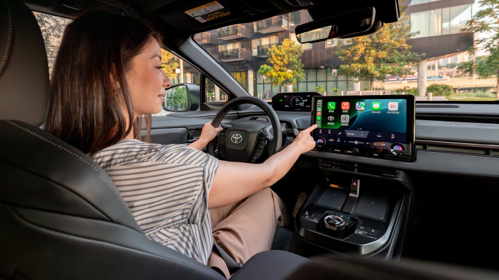 Person using touchscreen infotainment system inside a parked Toyota car with modern digital dashboard and controls.