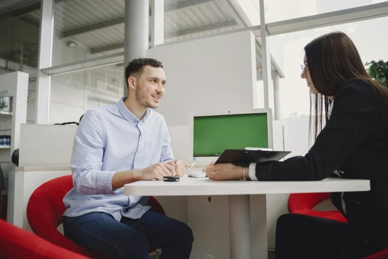 two people sitting at desk in dealership going over documents