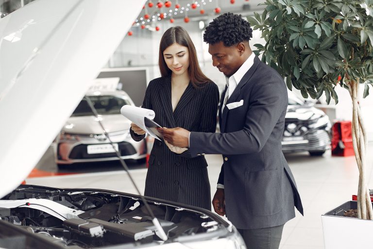 customers looking over paperwork in dealership infront of vehicle with hood popped open